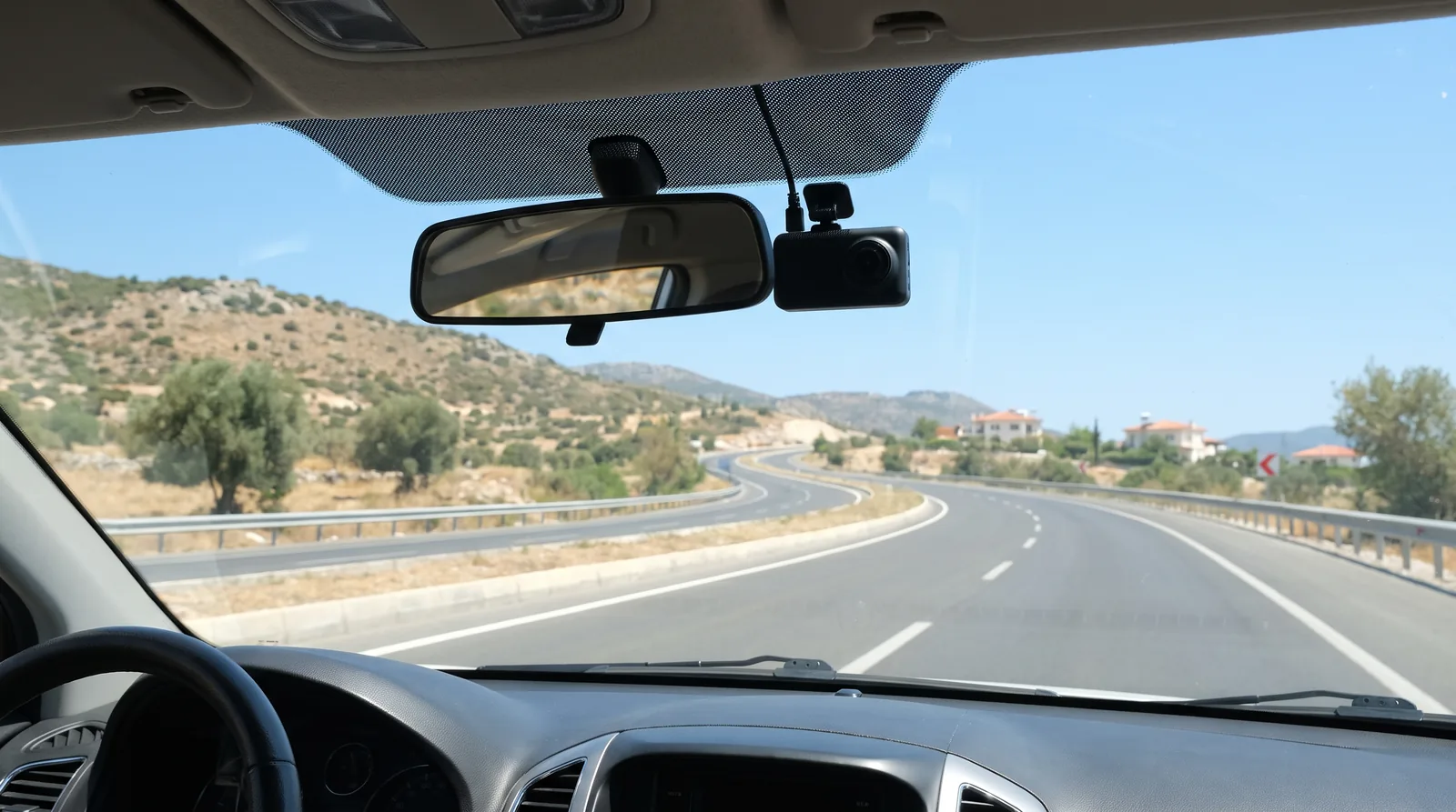 Araç içinden görünen açık gündüz yolu; dikiz aynası yanında sade bir araç kamerası